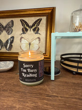 Load image into Gallery viewer, Candle with 'I'm Busy Reading' text on a shelf with a framed butterfly picture in the background.